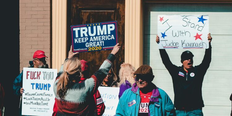 Trump gestures during a speech, with flags of the US and Canada in the background.