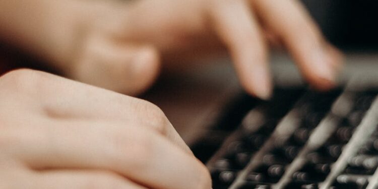 Hands typing on a laptop keyboard with digital currency symbols in the background.