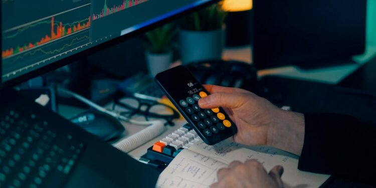 Kraken logo displayed on a computer screen with stock market charts and crypto graphics.
