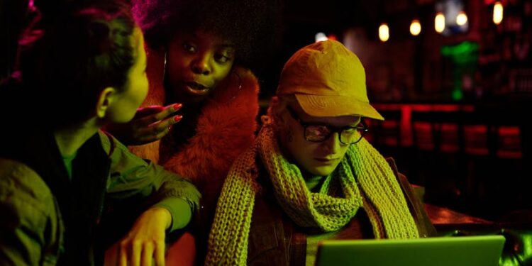 A group of diverse individuals discussing cryptocurrency on laptops at a café.