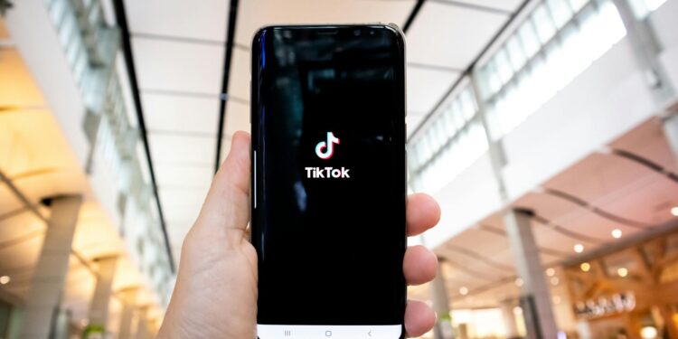 A smartphone displaying the Upscrolled app amidst TikTok logos and protest signs in Australia.