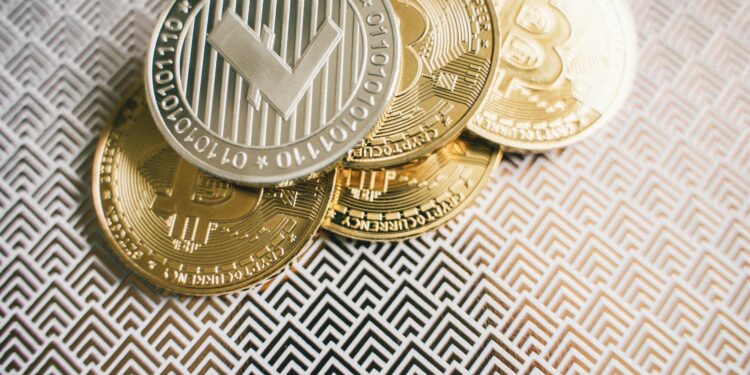 A trader analyzing cryptocurrency charts with gold and silver coins in the background.