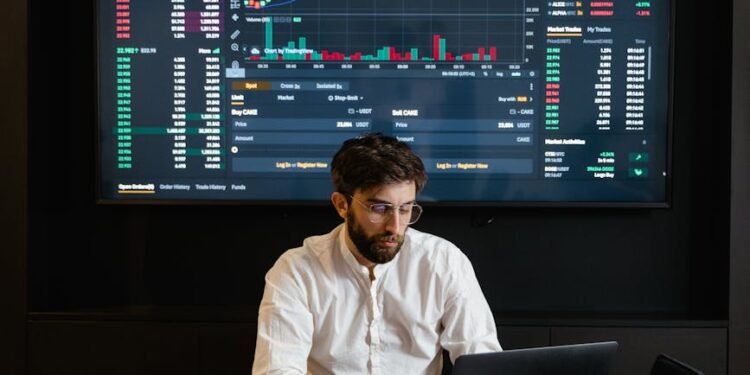 A trader monitors cryptocurrency charts on multiple screens in a modern office setting.