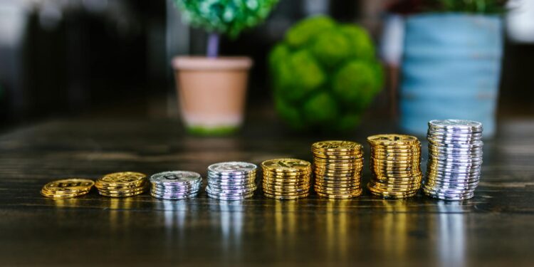 Gold and silver coins stacked with financial graphs illustrating market trends.