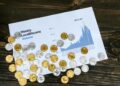 A person analyzing cryptocurrency charts on a laptop, with coins and financial reports nearby.