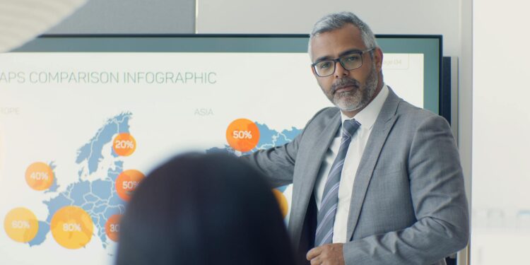 Coinbase CEO speaking at a conference with charts showing cryptocurrency trends behind him.