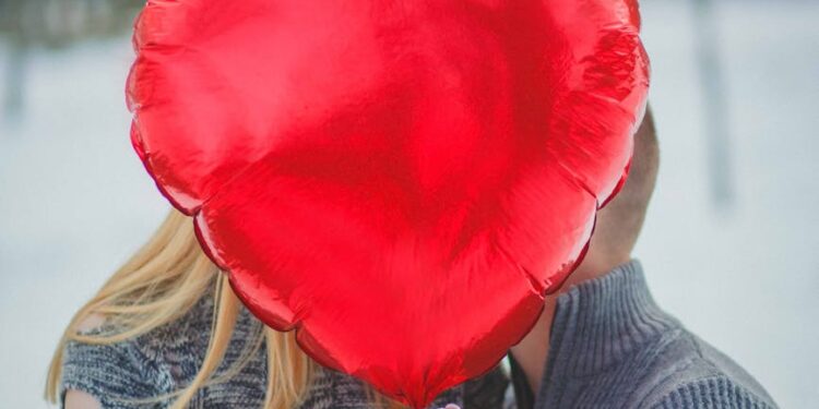 Couple holding hearts, with a laptop showing cryptocurrency icons in the background.