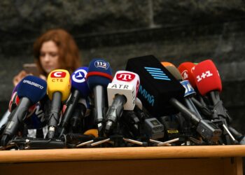 Telegram CEO in focus at a press conference, with a backdrop of a news report on terrorism links.