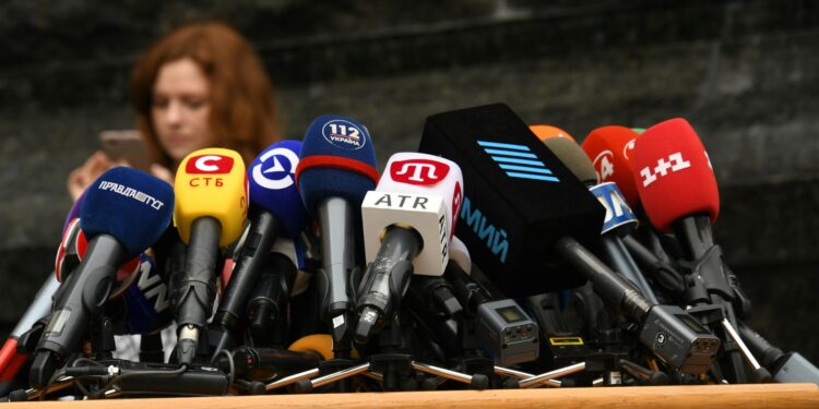 Telegram CEO in focus at a press conference, with a backdrop of a news report on terrorism links.