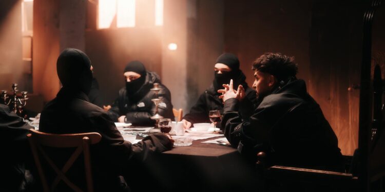 A group of cybercriminals strategizes over laptops with cryptocurrency logos in a dimly lit room.