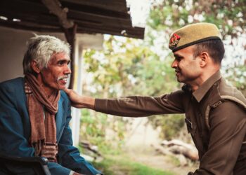 Police officer holding cryptocurrency symbols with an elderly person in the background.