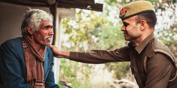 Police officer holding cryptocurrency symbols with an elderly person in the background.