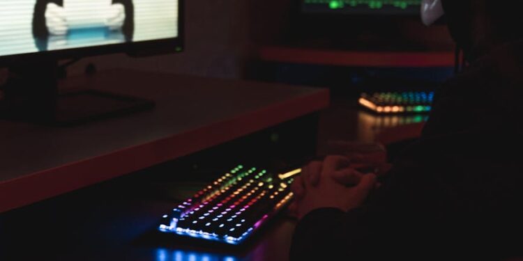 A hacker wearing a mask working on a computer with digital security graphics around.