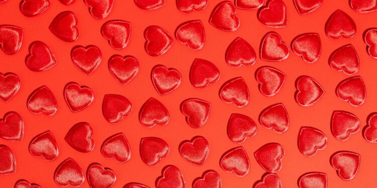 A smartphone displaying cryptocurrency icons next to a Valentine's Day heart graphic.