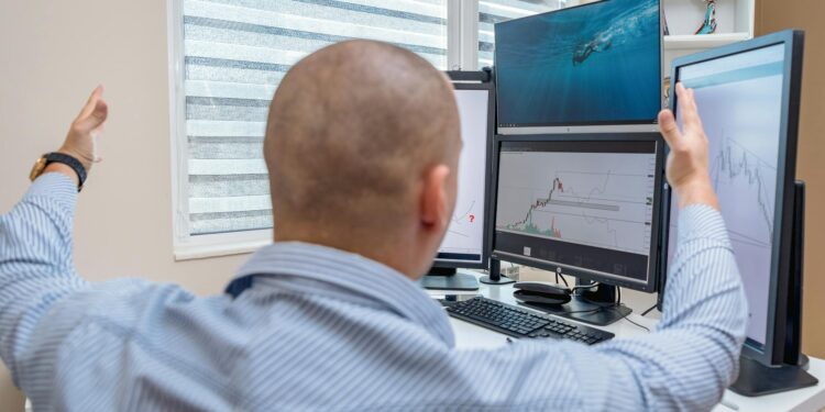 A trader monitors cryptocurrency charts on multiple screens in a financial setting.