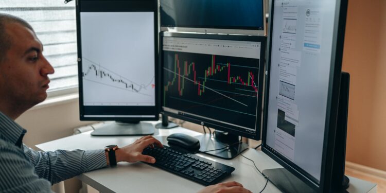 A trader analyzing financial charts on multiple screens with AI algorithms displayed.