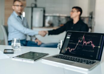 Business executives shaking hands with financial graphs and logos of Amazon and Nvidia in the background.