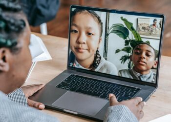 Students in a classroom learning about cryptocurrency with laptops and Bitcoin graphics on screen.