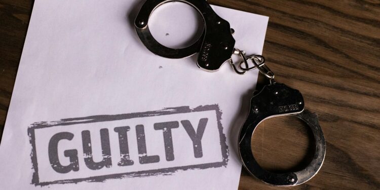 Defendant in handcuffs enters courtroom for sentencing in cryptocurrency fraud case.