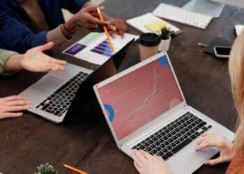 A diverse group of individuals discussing cryptocurrency with laptops and charts in a modern office.