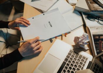 MrBeast's editor, under scrutiny, sits at a desk with financial documents and a laptop.