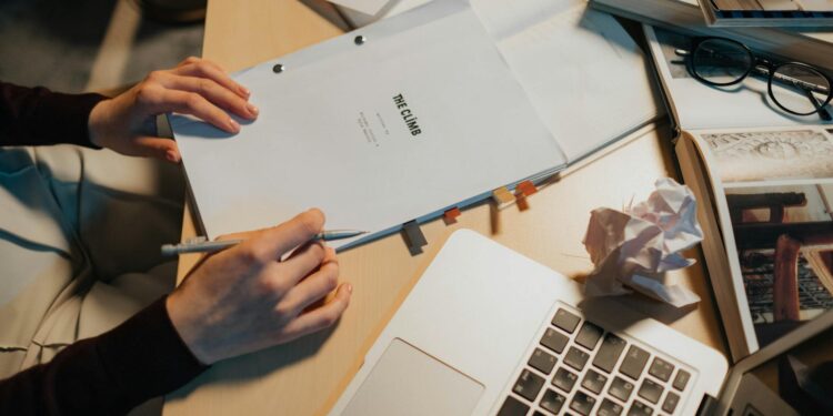 MrBeast's editor, under scrutiny, sits at a desk with financial documents and a laptop.