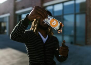 A person holding a cryptocurrency card with financial symbols in the background.