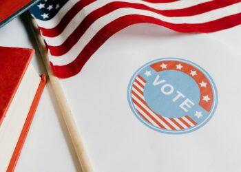 A representative holds a cryptocurrency symbol next to a financial chart and political campaign materials.