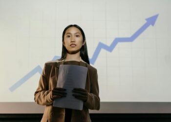 Christopher Delgado speaking at a financial conference, with crypto charts projected behind him.