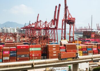 Two businessmen discuss blockchain technology at a cargo shipping terminal in Hong Kong.