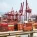 Two businessmen discuss blockchain technology at a cargo shipping terminal in Hong Kong.