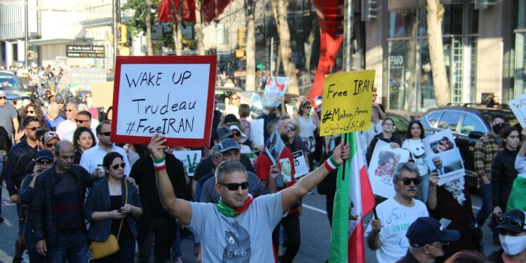 Demonstrators holding signs during protests in Iran, with darkened screens in the background.