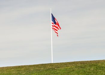 Cryptocurrency symbols and graphs with a backdrop of the US flag and sanctions document.