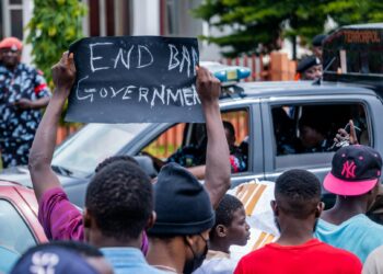 A protester holds a sign against AI military contracts outside a government building.