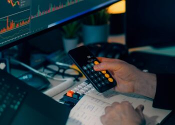 A stressed financial analyst reviews falling cryptocurrency charts on a computer screen.