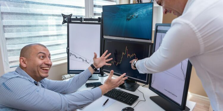 People celebrating in an office while analyzing financial graphs on screens.