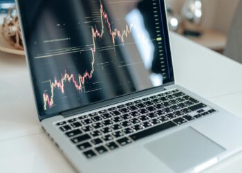 A financial analyst reviewing cryptocurrency market trends on a laptop in an office setting.