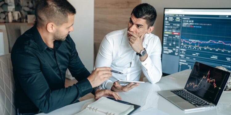Investors discussing cryptocurrency in a modern office setting, charts and laptops visible.