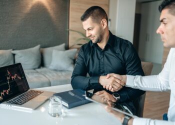 Investment handshake between two business professionals with digital stock graphs in the background.