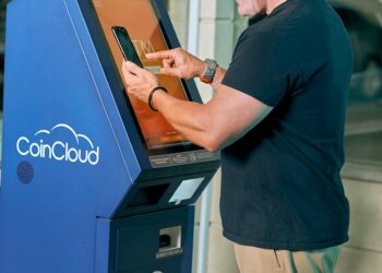 A person using a crypto ATM in a busy urban environment, surrounded by warning signs.