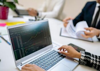 A business professional analyzes cryptocurrency charts on a laptop with financial documents nearby.