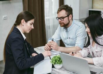 Two businesspeople discuss financial documents with cryptocurrency symbols in the background.