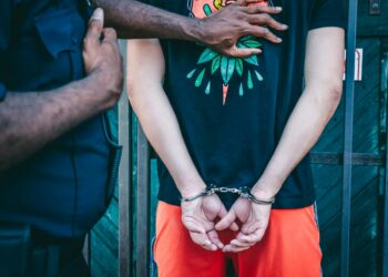A person in handcuffs being led away by law enforcement, with financial documents visible.