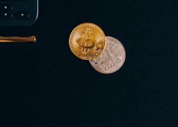 A stack of coins with Bitcoin and Ethereum logos beside a calculator and financial documents.