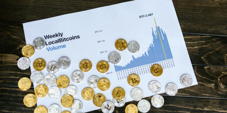 A Bitcoin coin sits on a fluctuating financial graph background with a downward trend.