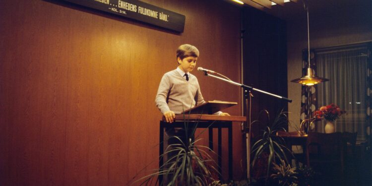 Japan PM Takaichi speaking at a podium with cryptocurrency graphics in the background.