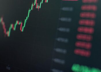 Oil barrels and a Bitcoin symbol overlaid on a stock market graph, highlighting volatility.