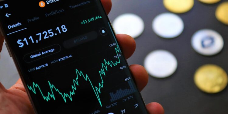 A person uses a smartphone to access cryptocurrency trading apps on a desk with financial documents.