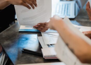 Group of people discussing cryptocurrency regulations around a table with laptops and documents.