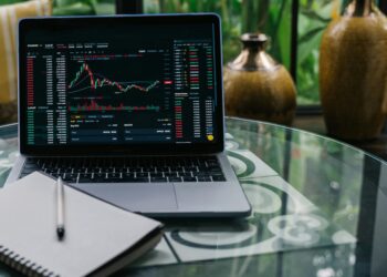 A person reviewing DeFi platforms on a laptop with financial charts and crypto symbols visible.